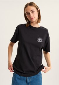 Camiseta de algodón negra con un corte relajado, cuello redondo y mangas cortas; presenta un estampado gráfico blanco de "VANS" y rayos de sol.