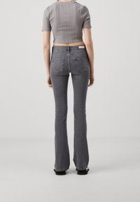 Jean acampanados grises con cintura media y dos bolsillos traseros, combinados con una camiseta corta de punto gris con mangas cortas.
