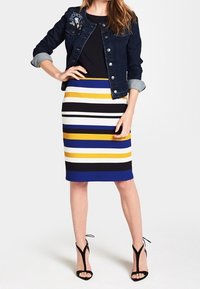 Denim jacket with embroidered details, black top, and striped pencil skirt in blue, yellow, white, and black. Black strappy heels.