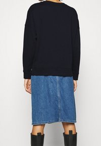 Sudadera azul marina con un corte holgado, puños y dobladillo acanalados, combinada con una falda de denim que presenta una costura central y un corte hasta la rodilla.