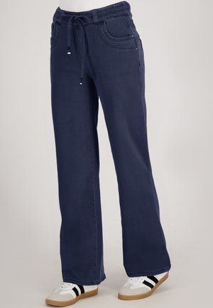 Navyblauwe wijde broek met elastische tailleband en trekkoord, gedragen met witte sneakers met zwarte strepen en gumrubberen zolen.