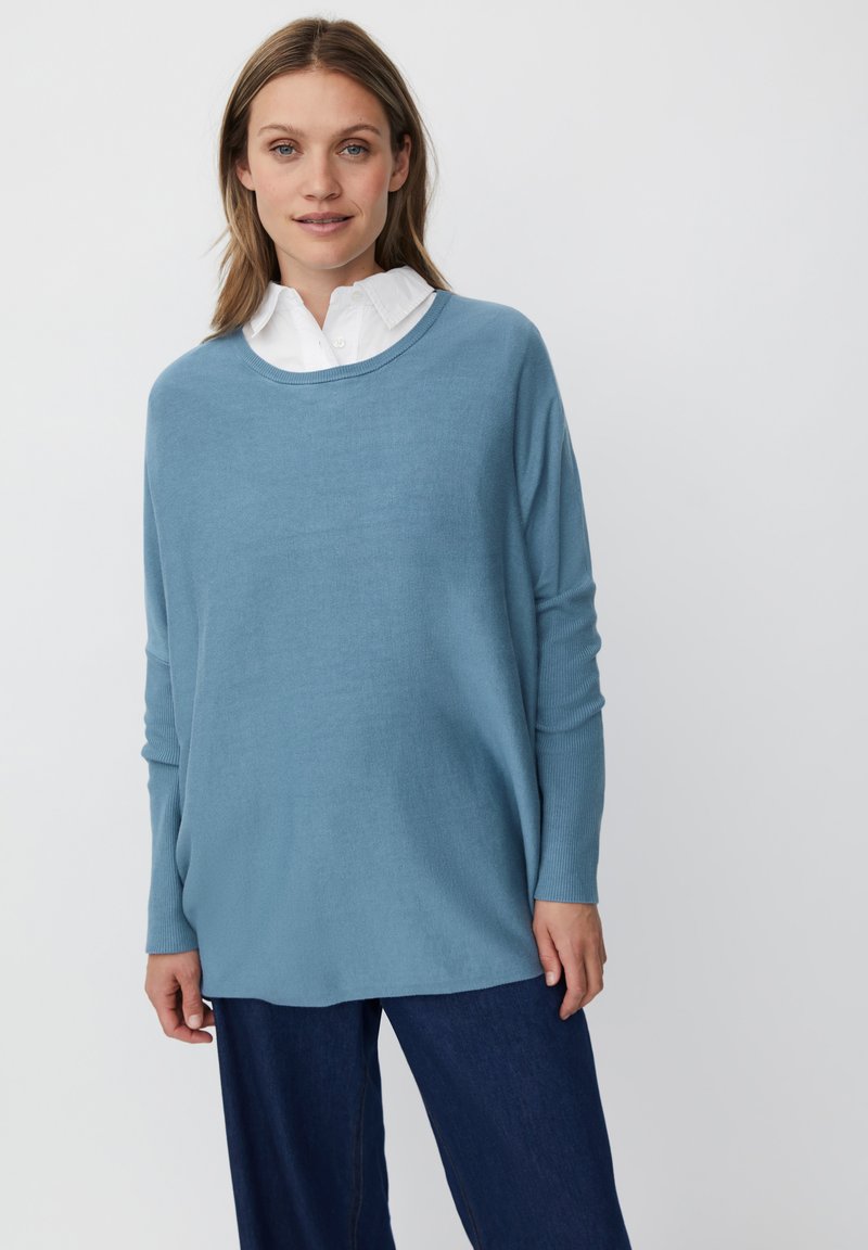 Jasnoniebieski, oversize sweter z okrągłym dekoltem i długimi rękawami, wykonany z miękkiego materiału. W połączeniu z ciemnoniebieskimi dżinsami, o minimalnej fakturze.