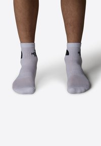 Calcetines deportivos blancos con puños acanalados, que cuentan con texto en negro en el tobillo y una textura de malla para transpirabilidad.