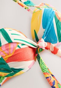 Haut de bikini à imprimé tropical coloré avec bonnets rembourrés et un détail de nœud à l'avant sur fond blanc.