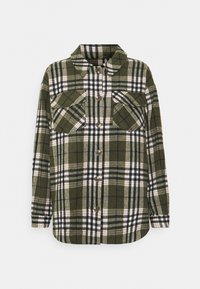 Chemise en flanelle à carreaux verts avec un col, deux poches poitrine, boutons marron, et un mélange de rayures blanches, noires et beige. Texture douce.