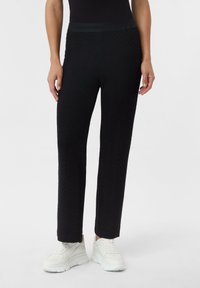 Czarne, teksturowane spodnie z wzorem w jodełkę, z gładkim pasem w talii i prostym krojem nogawek, zestawione z białymi trampkami.