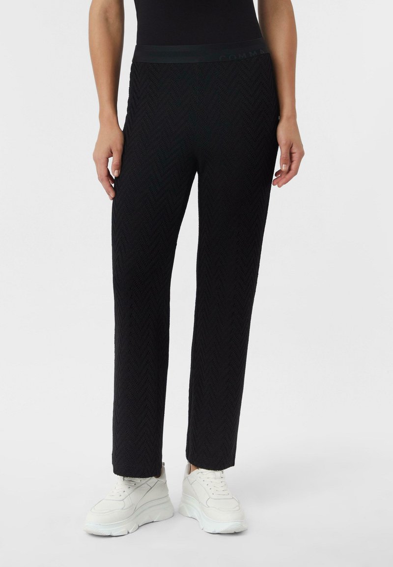 Czarne, teksturowane spodnie z wzorem w jodełkę, z gładkim pasem w talii i prostym krojem nogawek, zestawione z białymi trampkami.