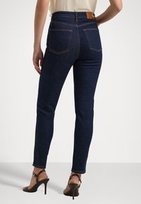 Mörkblå skinny jeans med hög midja, med sömdetaljer och bakfickor. Bärs med bruna remsandaler.