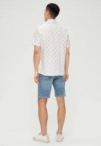 Kurzärmliges weißes Hemd mit kleinen blau-rot blumigen Mustern, kombiniert mit hellblauen Jeansshorts und weißen Sneakers, von hinten betrachtet.