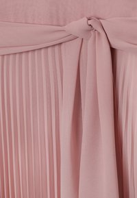 Tissu rose doux avec un détail de nœud en forme de ruban au-dessus d'une texture finement plissée, mettant en valeur les plis délicats et la finition lisse du matériau.