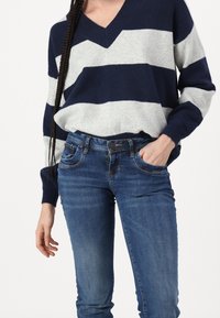 Pull en tricot rayé bleu marine et gris avec un décolleté en V, associé à un jean en denim bleu doté de cinq poches et d'une fermeture à bouton.
