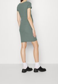 Grön ribbad kortärmad klänning med en figursydd silhuett, knälång fåll, kombinerad med svarta klackskor med blockklack och vita ankelsockor.