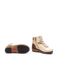 Bottines beiges avec un accent texturé marron clair, lacets à l'avant, fermeture éclair sur le côté et une semelle en caoutchouc marron crantée avec des motifs antidérapants.