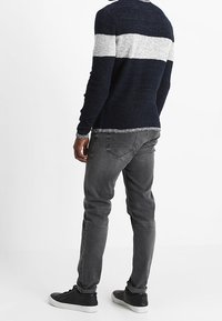 Pull bleu marine avec une bande blanche traversant la poitrine, associé à un jean gris slim et des baskets noires, vu de dos.