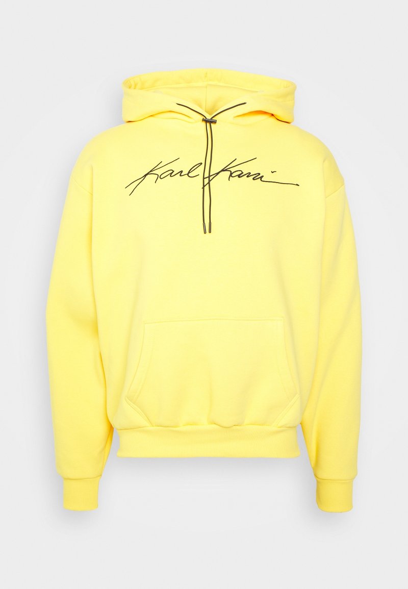 Sweat à capuche jaune avec cordons noirs et logo signature "Karl Kani" imprimé sur la poitrine, avec une poche kangourou à l'avant.