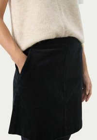 Zwarte corduroy mini-jurk met zijzakken, voorzien van een gestructureerd ribbelpatroon en een lichte uitloop aan de zoom.