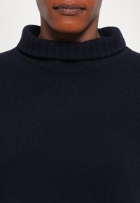 Zbliżenie na osobę w ciemnogranatowym, prążkowanym swetrze z golfem, ukazującym złożony kołnierz i teksturowany materiał dziany.