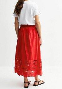 Jupe en coton rouge avec un motif découpé floral le long de l'ourlet, complétée par une ceinture élastique. Associée à un t-shirt blanc et des sandales.