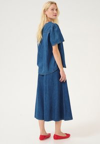 Denima tops un maksi svārki vienots zilā krāsā. Īsas piedurknes, brīva piegriezuma un izšūti akcenti. Spilgti sarkanas baleta kurpes papildina izskatu.