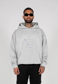 Grå hoodie med et forreste motiv af lilla sommerfugle. Har en hætte med snører og en kengurulomme. Bæres med sorte cargo shorts.