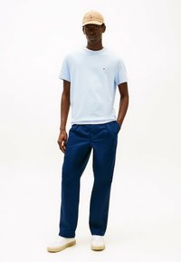 Camiseta de manga corta azul claro, pantalones navy, gorra beige con logo, zapatillas blancas. Ajuste casual, textura suave y sin patrones prominentes.