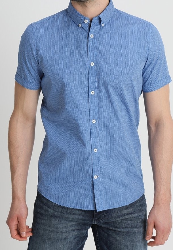 Homme portant une chemise bleue cintrée à manches courtes, boutonnée avec col boutonné, et un jean foncé.