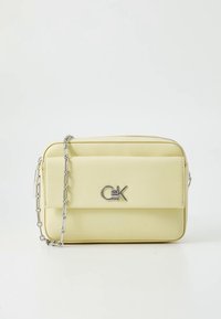 Sac bandoulière en cuir jaune avec ferrures en argent, fermeture éclair, poche avant à rabat et bandoulière chaîne. Design minimaliste et forme élégante.