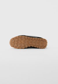 Semelle de chaussure en caoutchouc marron avec un motif carré et la marque "Armani Exchange" embossée au centre.