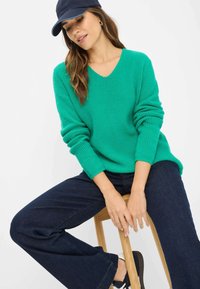 Grøn ribbet strikket sweater med V-hals, båret med mørkeblå vide bukser. En marineblå kasket og sneakers fuldender det afslappede outfit.