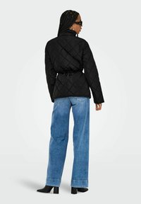 Veste matelassée noire avec une taille ceinturée, associée à un jean à jambe large bleu clair et des bottines noires à talons, vue de dos.