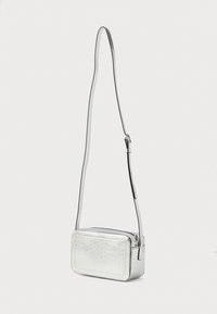 Strieborná crossbody taška s obdĺžnikovým tvarom, hladkým metalickým povrchom, nastaviteľným popruhom a zipsovým uzatváraním. Textúrovaný detail na prednej strane.