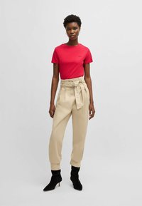 T-shirt rosso a maniche corte abbinato a pantaloni beige a vita alta con cintura. Il modello indossa stivaletti neri con tacco a spillo.
