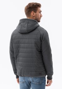 Chaqueta de plumas gris con capucha, que presenta un diseño acolchado en la parte trasera y un tejido liso de un gris más oscuro en las mangas y la capucha.