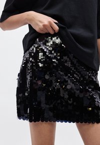 Czarna mini spódnica z cekinami o dopasowanym kroju, błyszczącymi okrągłymi cekinami w różnych odcieniach oraz gładką, refleksyjną teksturą.