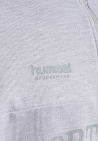 Ljusgrå sweatshirt med en strukturerad tyg. Har en subtil logotyp i grönt, dragkedjestängning och platta sömmar för en snygg finish.
