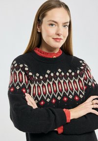 Pull noir avec un motif géométrique rouge et crème sur le dessus. Superposé avec une blouse rouge à col en dessous. Texture douce.