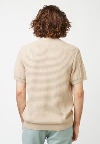 Chemise beige clair à manches courtes avec un motif texturé, des poignets et un ourlet côtelés, et un col classique, fabriquée dans un tissu tricot doux.