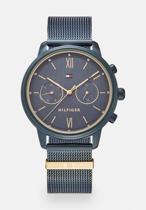 Dunkelblauer Armbanduhr mit goldenen Akzenten, Mesh-Armband, Markenname "Hilfiger", römische Ziffern bei 12 und 6 und zwei Hilfszifferblätter, die Tag und Datum anzeigen.