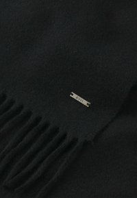 Sciarpa in lana nera con bordi frangiati e un'etichetta metallica del marchio fissata su un lato, che presenta una texture morbida.