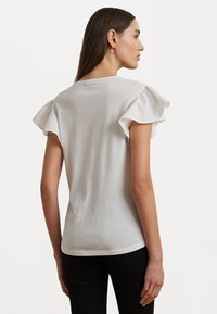 White cotton t-shirt with short ruffled sleeves, fitted design, and a round neckline, shown from the back against a plain background.