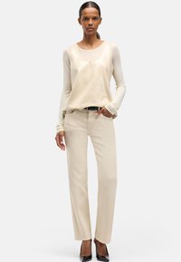 Beżowa cekinowa bluzka nałożona na jasnobeżową koszulę z długim rękawem, zestawiona z beżowymi spodniami o prostych nogawkach i czarnymi szpilkami z wąskimi noskami.