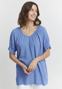 Top azzurro chiaro con maniche corte a volant e scollatura a V ampia. Realizzato in tessuto morbido, presenta una leggera texture e una vestibilità comoda.