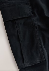 Primo piano della gamba di un pantalone cargo in tessuto nero con tasca rettangolare cucita e patta.