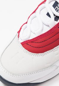 Białe sneakersy z czerwono-granatowym wzorem z teksturowanymi akcentami. Zawierają białe sznurówki i wypukłe logo z boku.