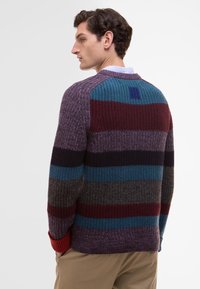 Knitted sweater with multicolored stripes in purple, teal, burgundy, and gray. Features ribbed cuffs and a textured finish.