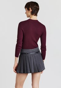 Haut à manches longues côtelé bordeaux associé à une jupe plissée gris foncé, dotée d'une taille ajustée et d'un éclat subtil.