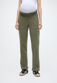 Εγκυμοσύνης παντελόνι σε ελαιόχρωμο ύφασμα με βολάν στη μέση, άνετη εφαρμογή και πλαϊνές τσέπες, συνδυασμένο με μαύρα αθλητικά παπούτσια.