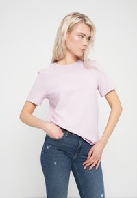 Ανοιχτό μωβ βαμβακερό T-shirt με λαιμόκοψη χαμηλή και κοντά μανίκια, συνδυασμένο με φθαρμένα μπλε τζιν. Απλή, ομαλή υφή.