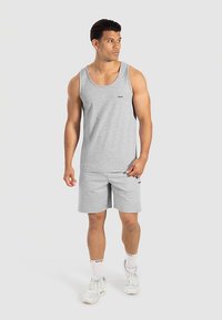 Lichtgrijs sportief tanktop- en shortsetje van gestructureerde stof. Opvallend logo detail aan de voorkant. Gecombineerd met witte sneakers en sokken.