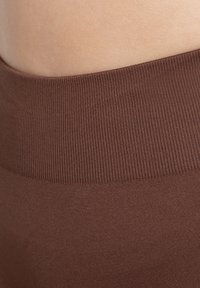 Brun elastisk midjeresår på ett plagg, med ribbad textur och slät tyg. Närbild som betonar färg och material.
